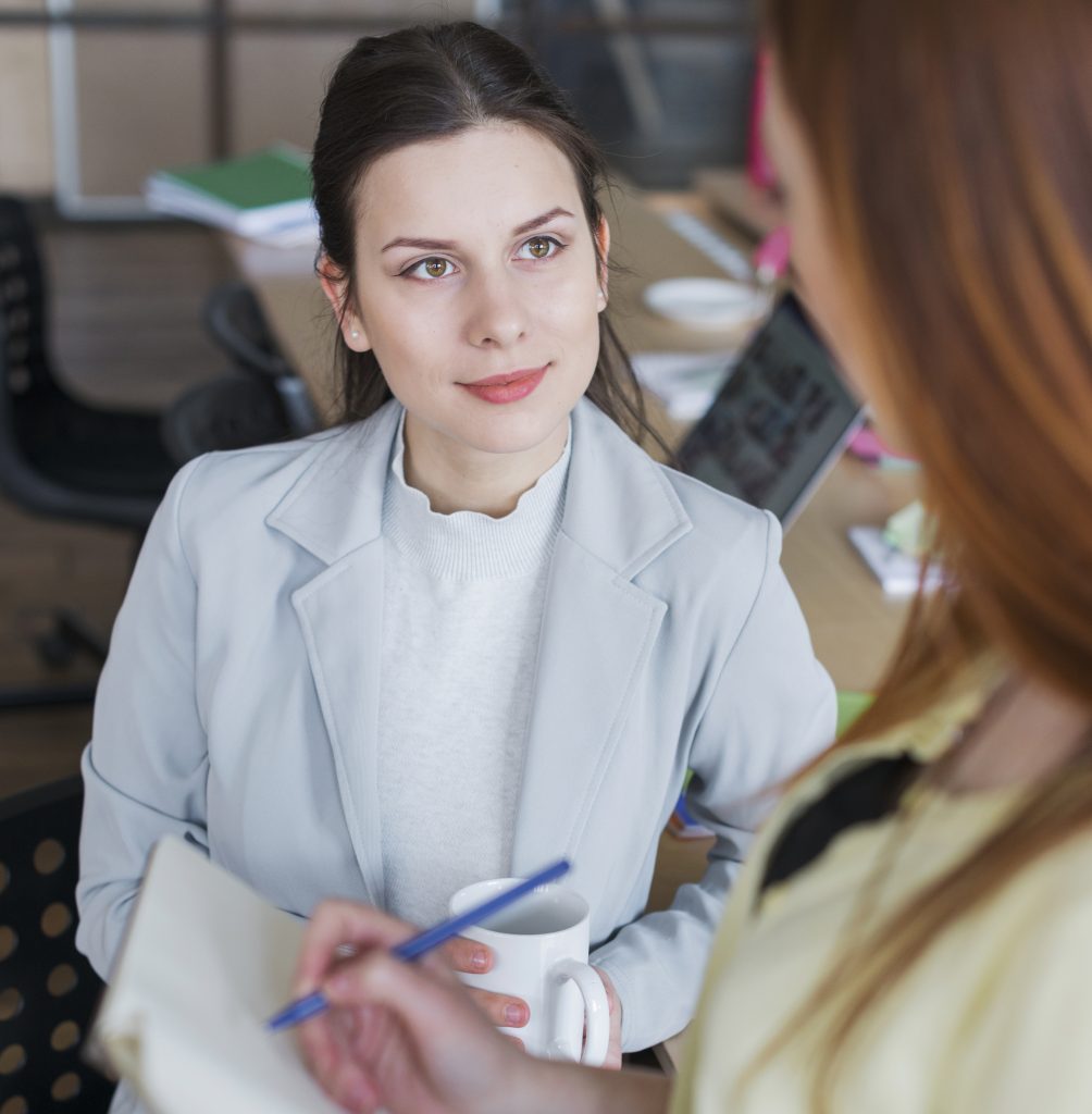 portrait-woman-sitting-chair-holding-coffee-cup-looking-her-colleague